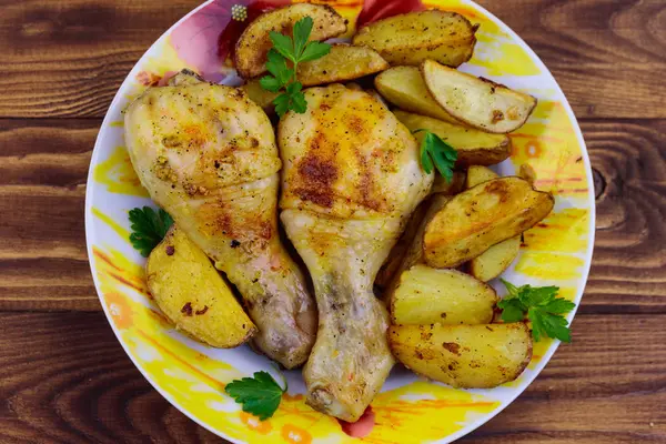 Gebakken kip drumsticks met aardappelen in een bord op houten tafel — Stockfoto