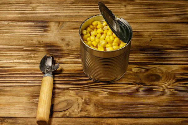 Open tin can of corn and can opener on wooden table — Stock Photo, Image