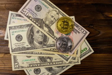 Ahşap masada altın ve gümüş bitcoinler ve dolar banknotları