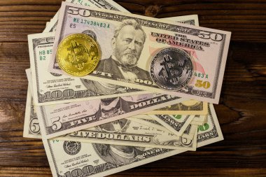 Ahşap masada altın ve gümüş bitcoinler ve dolar banknotları