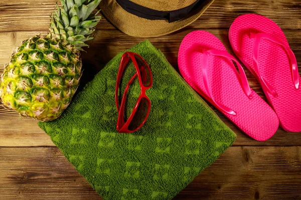 Sommerferienkonzept. Ananas, Strohhut, Flip-Flops, Handtuch und Sonnenbrille auf Holzgrund — Stockfoto