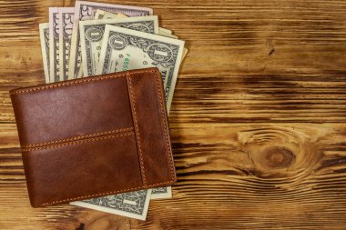 Kahverengi deri cüzdan ve ahşap masada Amerikan doları. Üst görünüm