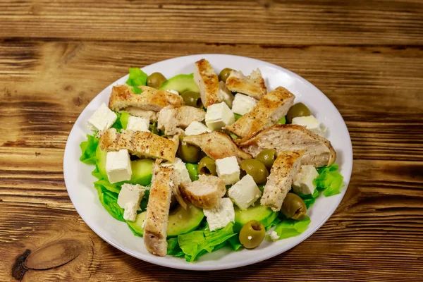Schmackhafter Salat mit gebratener Hühnerbrust, grünen Oliven, Feta-Käse, Avocado, Salat und Olivenöl auf Holztisch — Stockfoto