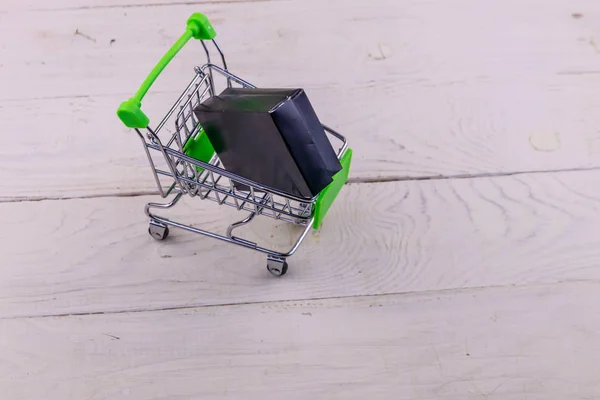 Carrinho de compras com caixa preta em fundo de madeira branca — Fotografia de Stock