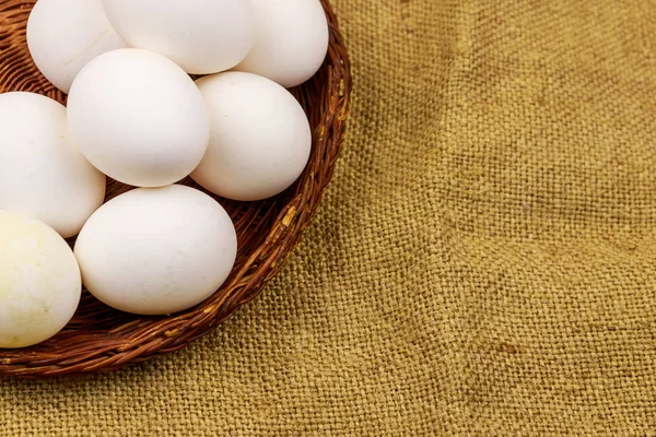 White chicken eggs in wicker basket on sackcloth background — Stock Photo, Image