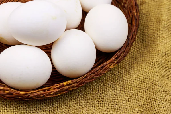 White chicken eggs in wicker basket on sackcloth background — Stock Photo, Image