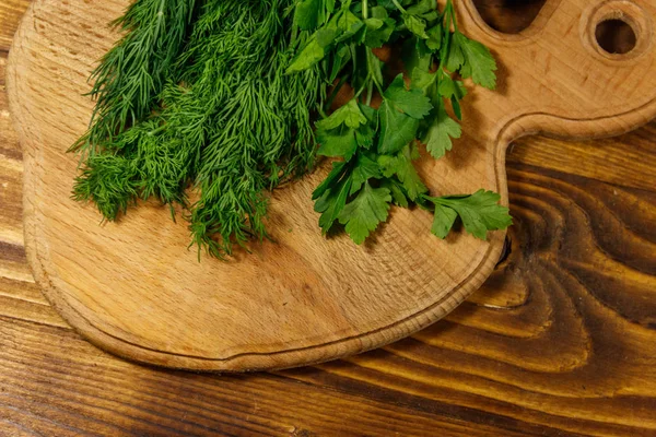 Eneldo verde fresco y perejil en tabla de cortar en mesa de madera —  Fotos de Stock