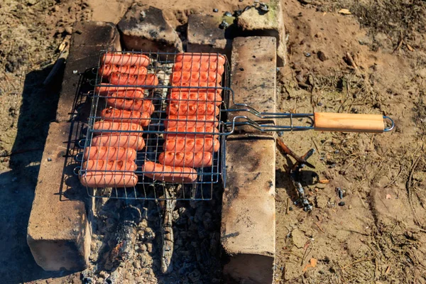 Grilling sausages in barbecue grill cooking on campfire — Stock Photo, Image