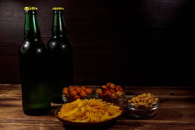 Bira şişeleri ve ahşap masada bira için çeşitli atıştırmalıklar.