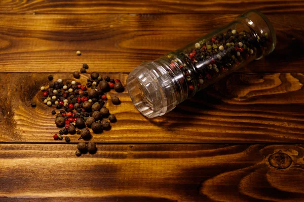 Glass pepper shaker with mix of peppercorn on wooden background