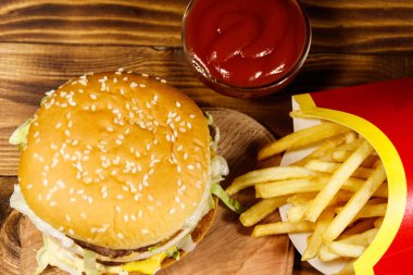 Ahşap masada patates kızartması ve ketçap ile lezzetli büyük hamburger. Üst görünüm
