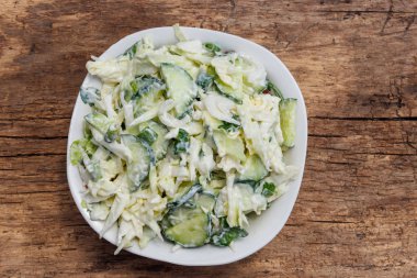 Ahşap masada lahana, salatalık, yeşil soğan, maydanoz ve mayonez ile bahar salatası. Üst görünüm