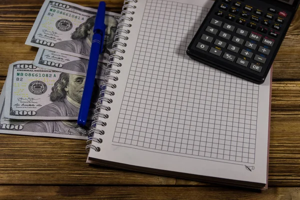 Notitieboekje met dollars, pen en Rekenmachine op houten bureau — Stockfoto