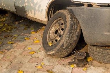Tamir için beyaz bir arabanın yanındaki eski tekerlek.