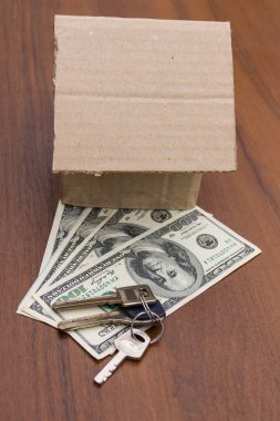 Ahşap masada küçük karton ev, anahtarlar ve dolar