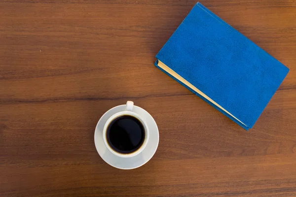Чашка кофе и закрытая книга на деревянном столе — стоковое фото