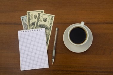Fincan kahve, dolar, not defteri ve kalem ahşap masa