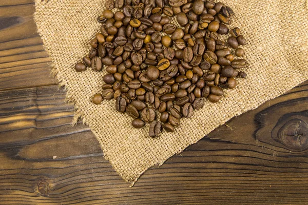 Prażone ziarna kawy na worze na drewnianym stole — Zdjęcie stockowe