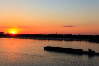Römorkör, gün batımında Dinyeper nehrinde ağır, uzun bir mavnayı itiyor.