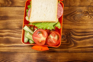 Sandviç ve ahşap masa üzerinde taze sebze ile okul beslenme çantası. Üstten görünüm