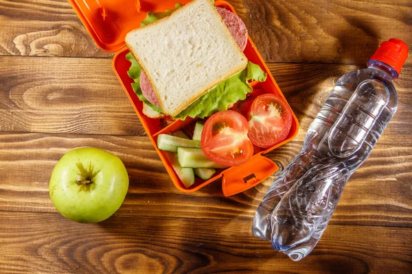 Pranzo scolastico con panino e verdure fresche, bottiglia d'acqua e mela verde sul tavolo di legno. Un concetto di alimentazione sana. Vista dall'alto — Foto Stock