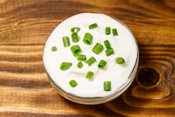 Crema agria con cebolla verde en cuenco de vidrio sobre mesa de madera —  Fotos de Stock
