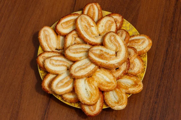 Palmier keksz - francia süti készült leveles tészta (is úgynevezett pálmalevél, elefánt fülek, vagy szívek francia) egy fából készült asztal a lemez — Stock Fotó