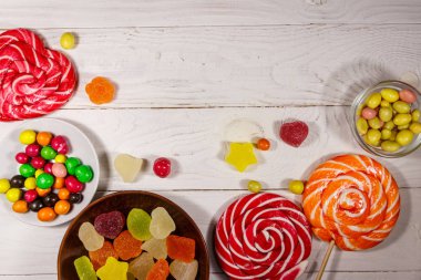 Renkli çikolatalı şekerler, lolipoplar ve jöleli şekerler beyaz ahşap masada.