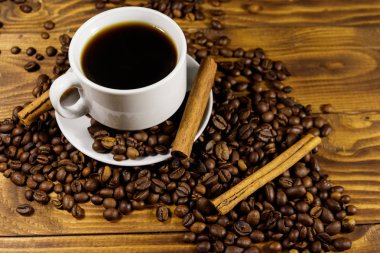 Bir fincan kahve, kavrulmuş kahve çekirdekleri ve ahşap masada tarçın çubukları.