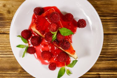Ahşap masa üzerinde beyaz bir tabakta ahududu ve ahududu reçeli ile lezzetli New York cheesecake Parçası. Üstte görüntü