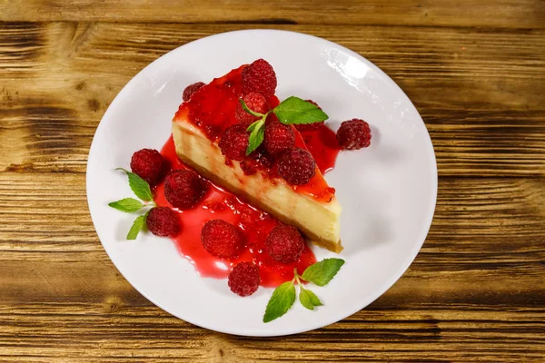 Piece of tasty New York cheesecake with raspberries and raspberry jam in a white plate on wooden table — Stock Photo, Image