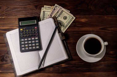 Bir fincan kahve ve dolar, kalem ve hesap makinesi olan bir not defteri. Mali konsept