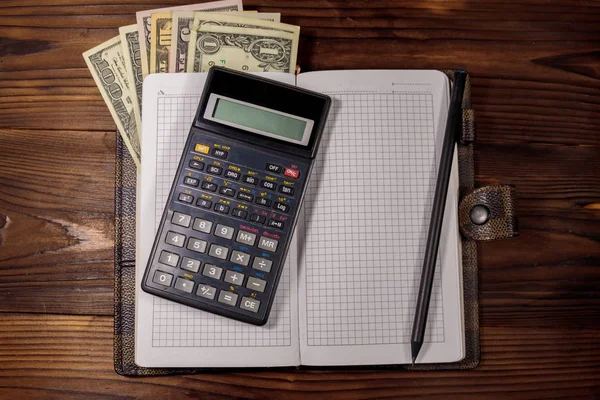 Notitieblok met dollars, potlood en rekenmachine op houten bureau. Begrip financiële planning — Stockfoto