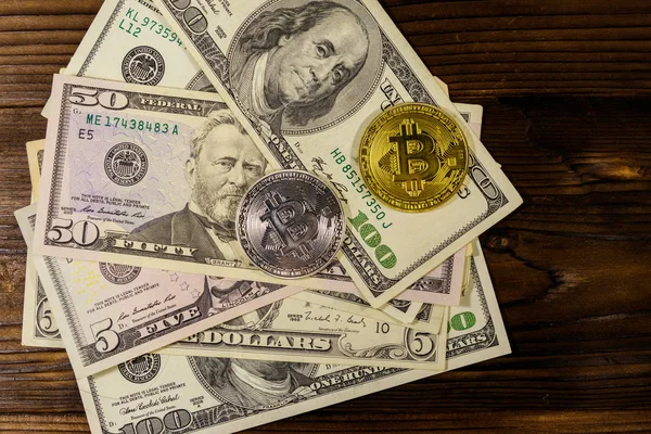 Ahşap masada altın ve gümüş bitcoinler ve dolar banknotları