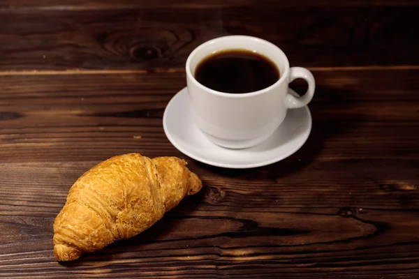 一杯のコーヒーと木製のテーブルに新鮮なクロワッサン — ストック写真