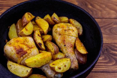 Ahşap masa üzerinde dökme demir tavada patates ile Fırında tavuk drumsticks