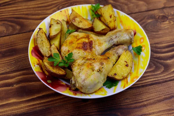 Gebakken kip drumsticks met aardappelen in een bord op houten tafel — Stockfoto