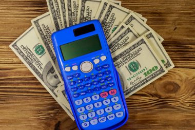 Hesap makinesi ve ahşap masanın üzerine amerikan doları banknotlar. Üstte görüntü