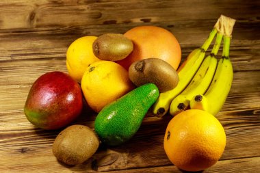 Ahşap masa üzerinde tropikal meyve çeşitleri. Muz, mango, portakal, avokado, greyfurt ve kivi ile natürmort