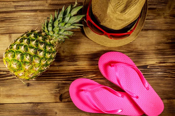 Концепция летнего отдыха. Ананас, соломенная шляпа, шлепанцы и солнечные очки на деревянном фоне — стоковое фото