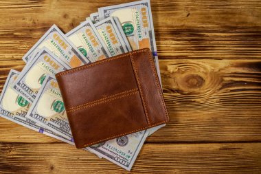 Kahverengi deri cüzdan ve ahşap masada Amerikan doları. Üst görünüm