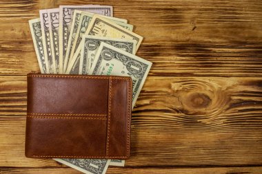 Kahverengi deri cüzdan ve ahşap masada Amerikan doları. Üst görünüm