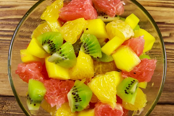 Smakelijke fruitsalade in glazen kom op de houten tafel — Stockfoto