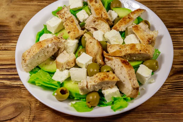 Salada saborosa com peito de frango frito, azeitonas verdes, queijo feta, abacate, alface e azeite em mesa de madeira — Fotografia de Stock