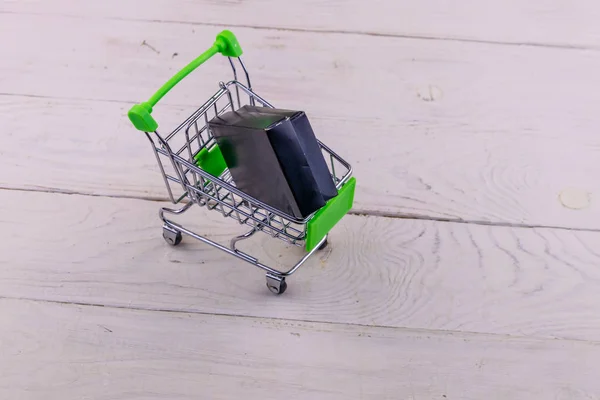 Carrito con caja negra sobre fondo de madera blanco —  Fotos de Stock