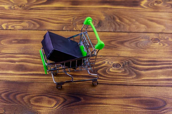 Carrito con caja negra sobre fondo de madera —  Fotos de Stock