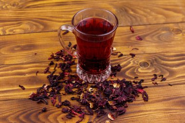 Ahşap masada bir bardak kırmızı amber çayı (carcade, roselle).