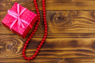 Ahşap arka plan üzerinde hediye kutusu ve kırmızı boncuk kolye