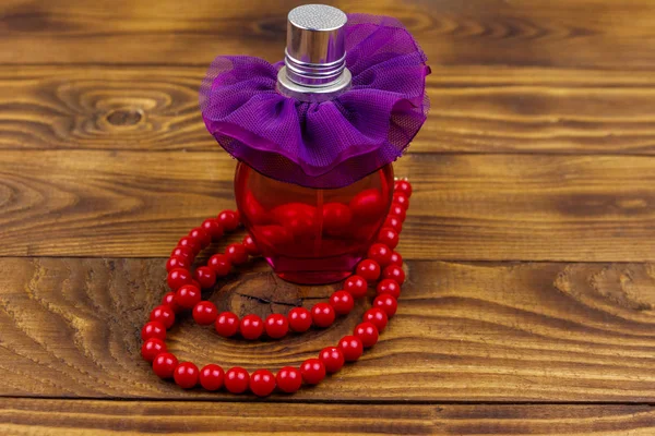 Bottle of perfume and red beads necklace on wooden background — Stock Photo, Image