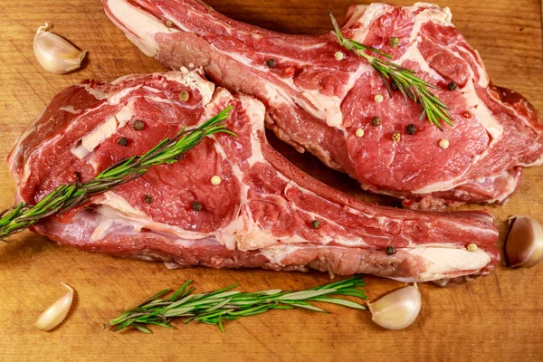 Raw fresh beef rib eye steak on bone with spices, garlic and rosemary on wooden table. Top view — Stock Photo, Image